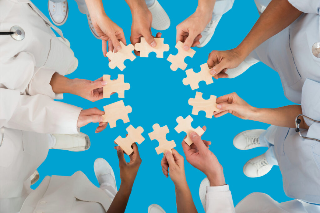 Directly above shot of medical team holding blue jigsaw pieces in huddle against white background